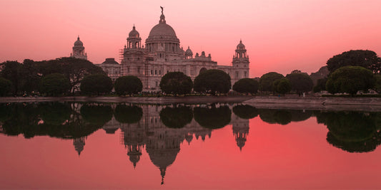 A photograph in pink tones featuring a white monument structure surrounded by trees, reflected in the lake in the foreground